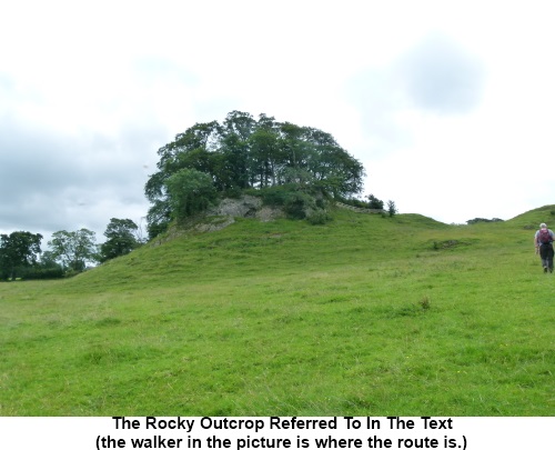 A tree covered rocky outcrop. The route passes to its right.